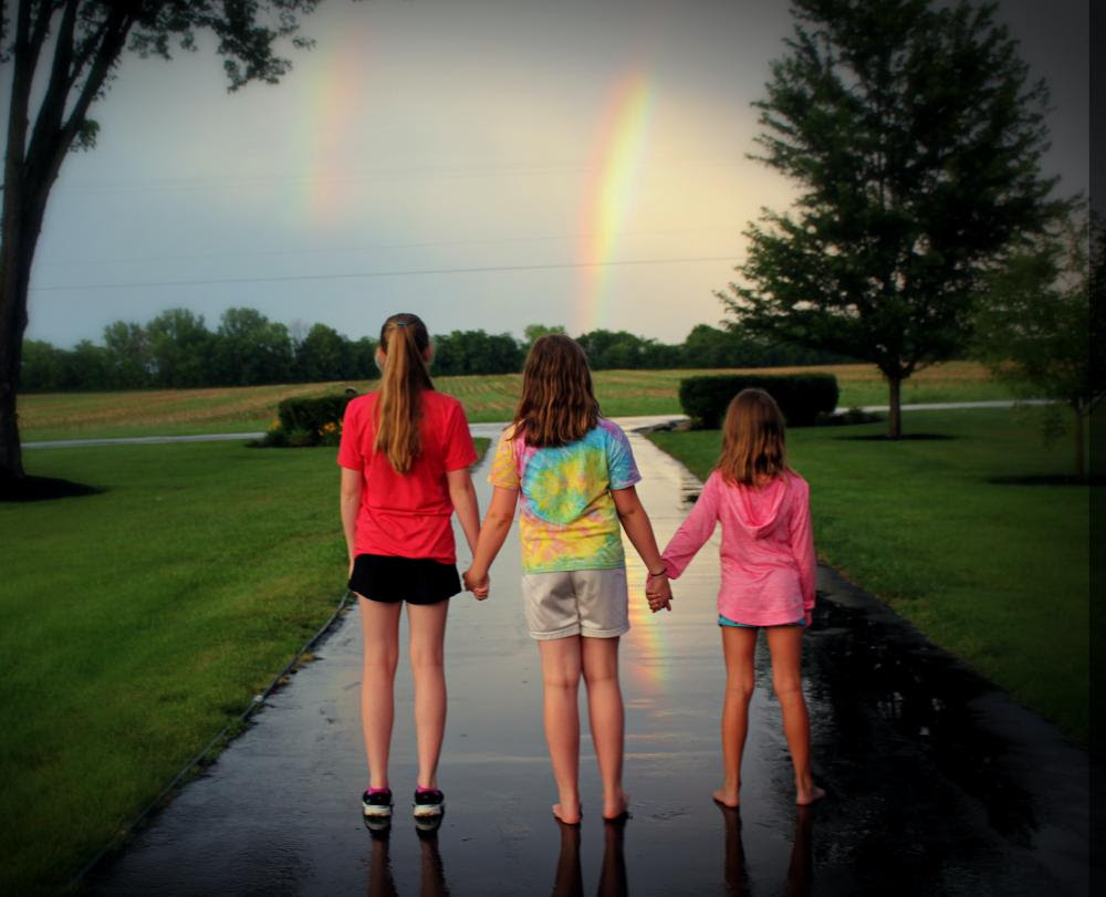 Kids holding hands in front of rainbow
